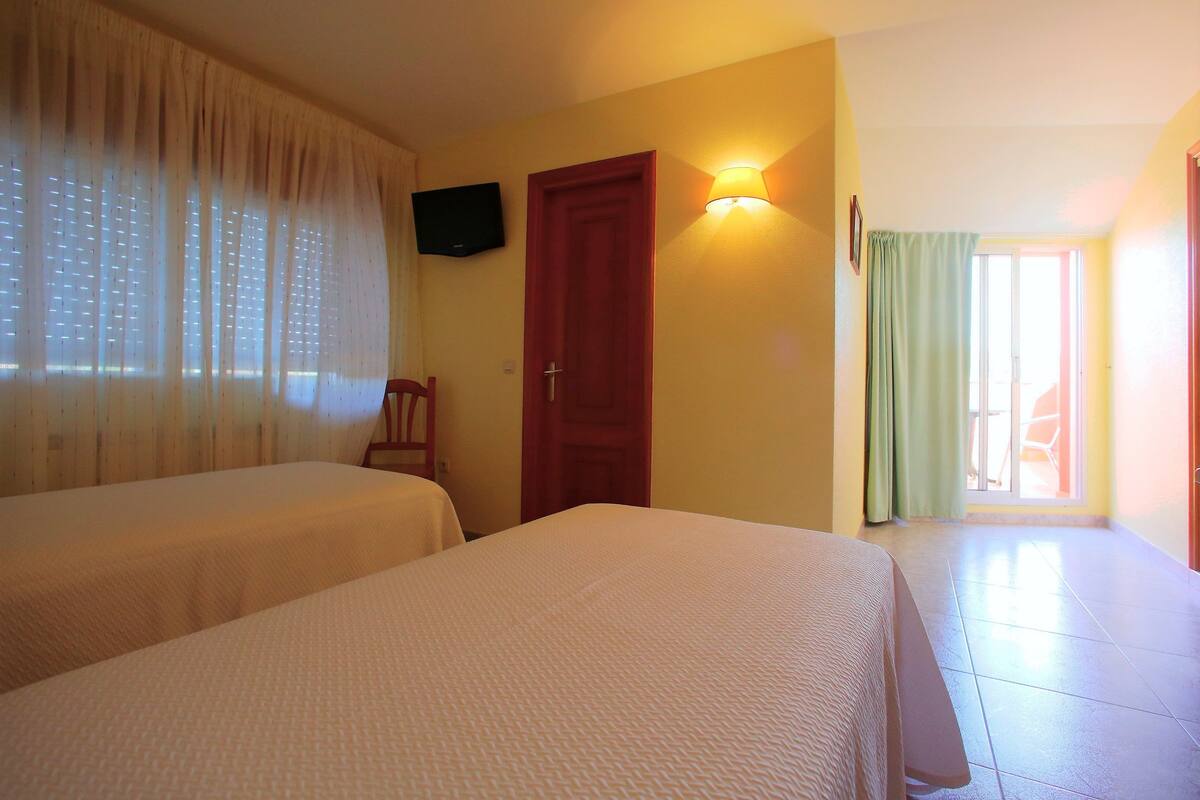 Habitación de hotel con dos camas, un televisor en la pared, una puerta y una ventana con cortinas.