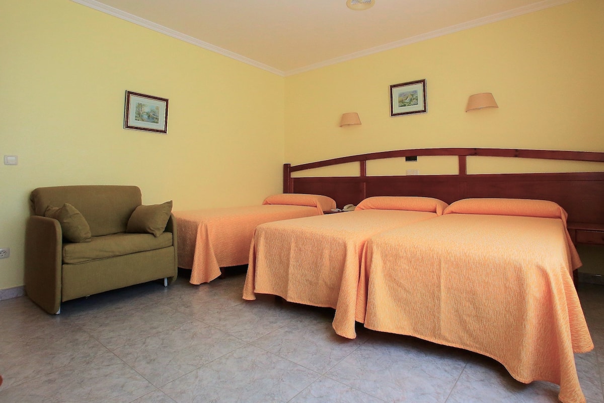 Habitación de hotel con dos camas individuales, un sofá y dos lámparas fijadas a la pared.