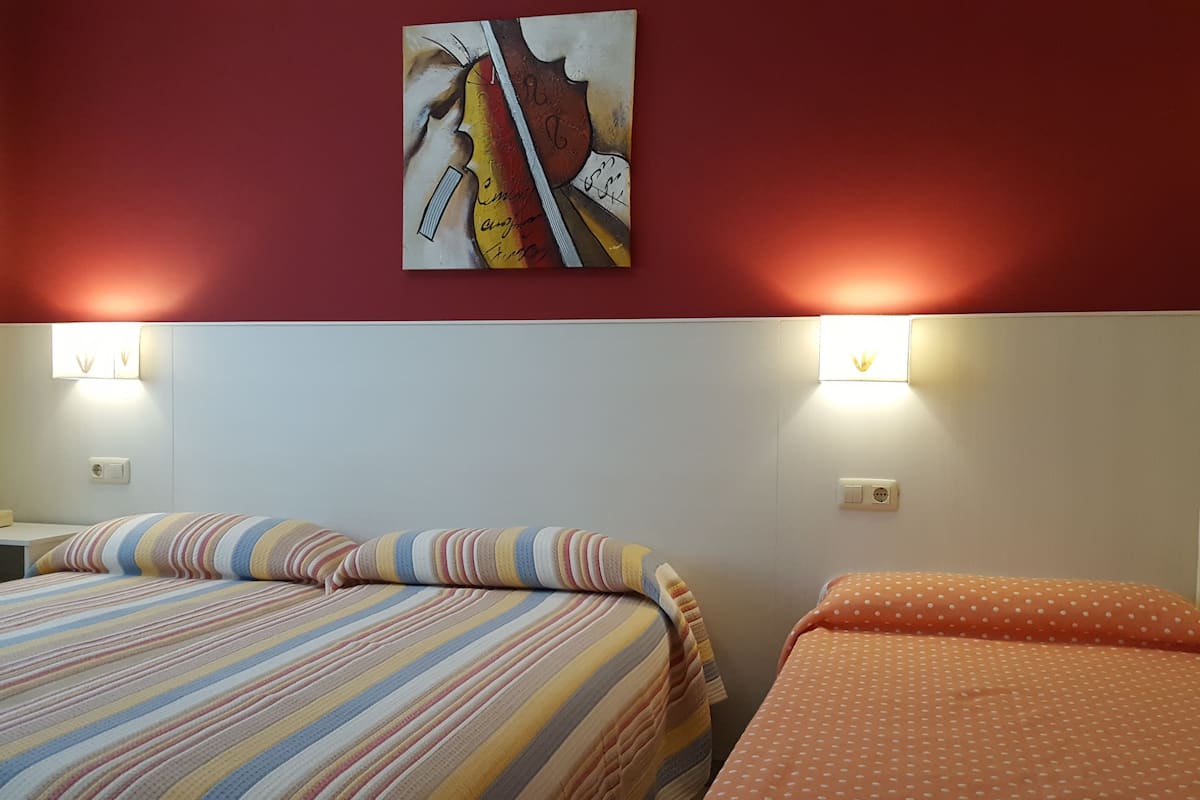 Habitación de hotel con dos camas, ropa de cama a rayas y con lunares, y un cuadro en la pared.