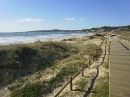 Una pasarela de madera a lo largo de una playa, con vista clara al océano y colinas al lejano.