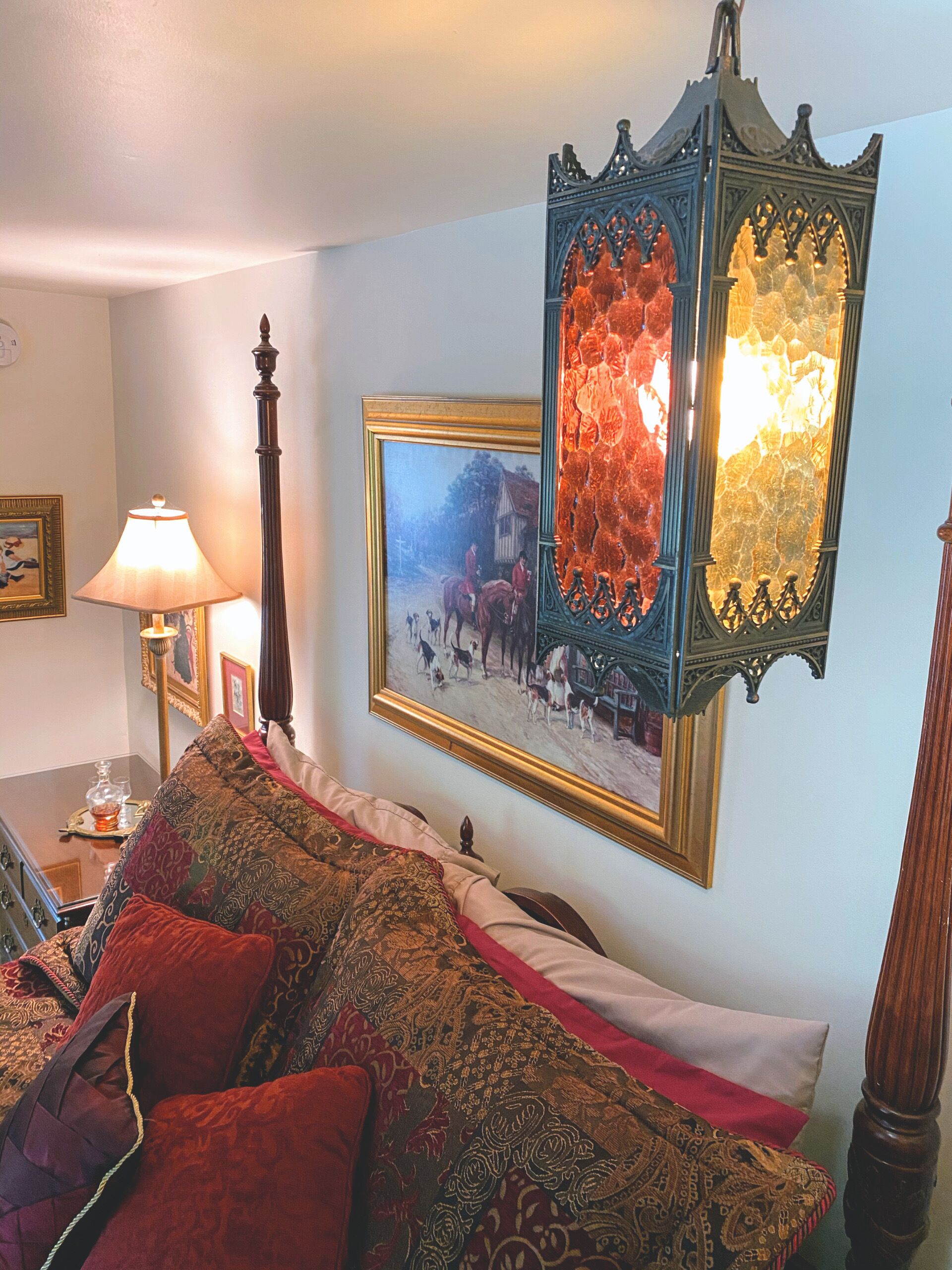 Quarto com cama, abajur, quadro emoldurado e espelho decorativo.