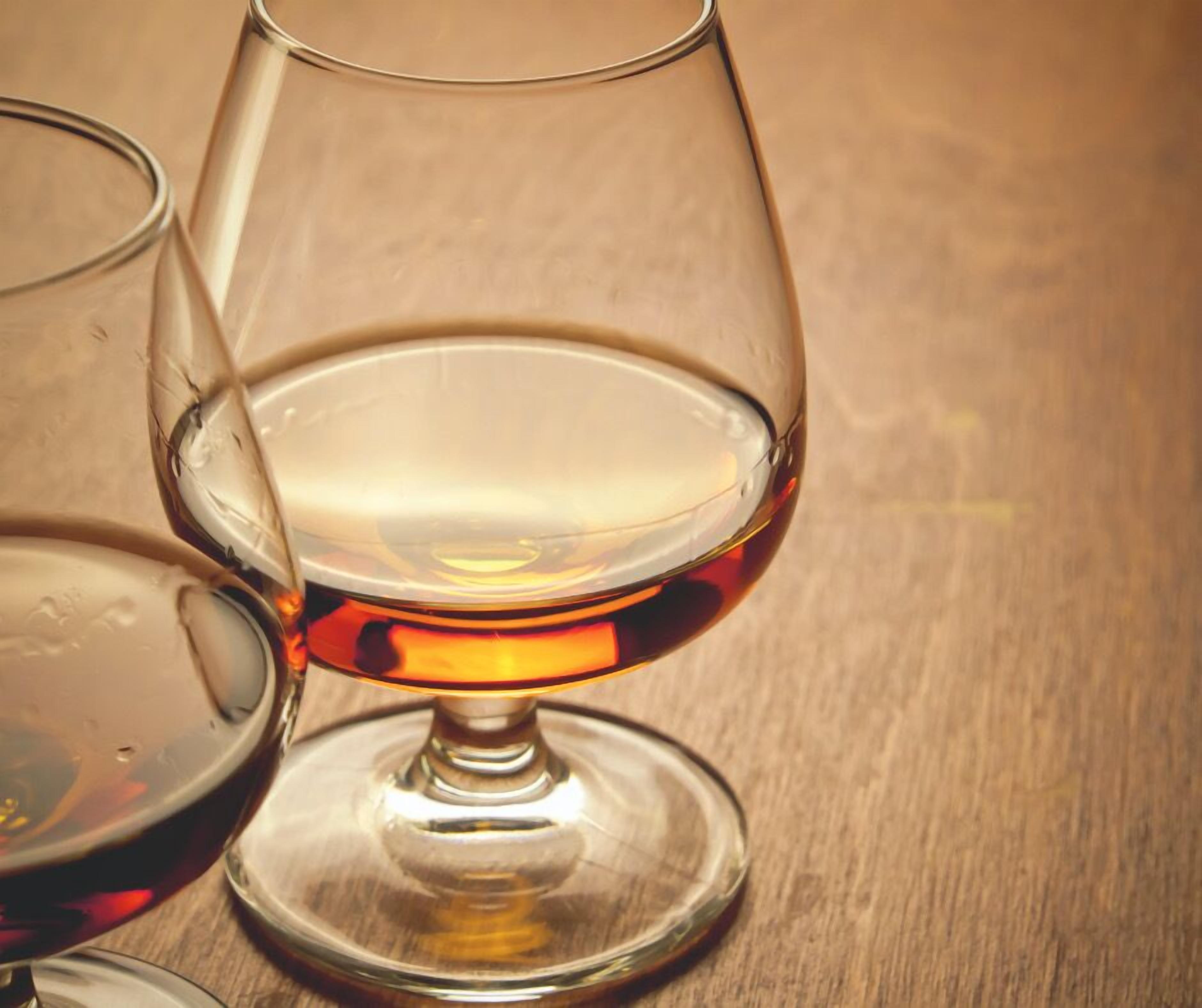 A glass of amber-colored liquid, possibly whiskey, on a wooden surface.