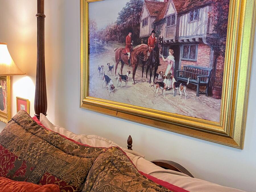 Una habitación con un cuadro grande enmarco de una escena histórica, una cama de madera con cabecera tallada y un plaid estampado en el sofá.