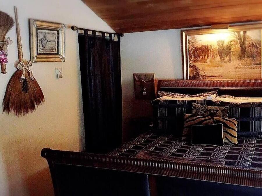 A room with a bed, a wooden ceiling, a painting, and a wall-mounted clock.