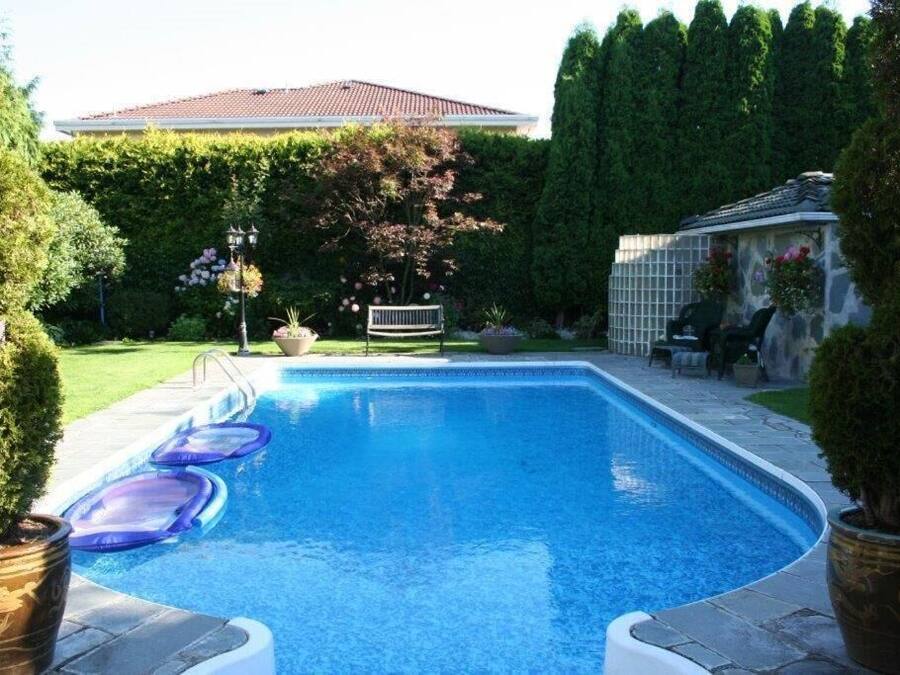 A swimming pool with a tiled deck, surrounded by well-maintained hedges and a stone wall.