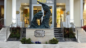 De ingang van een hotel met een opvallend bronzen beeld van twee figuren, een bord boven de ingang en een trap die naar de deur leidt.