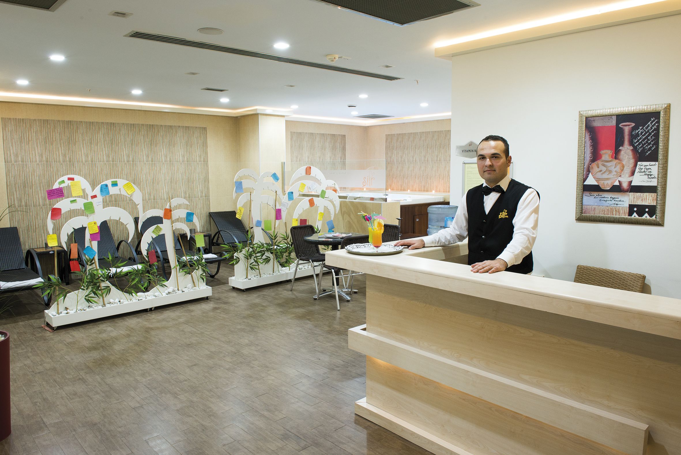 Uma área de recepção de hotel com design moderno, incluindo balcão de atendimento, espaço para assentos e elementos decorativos.