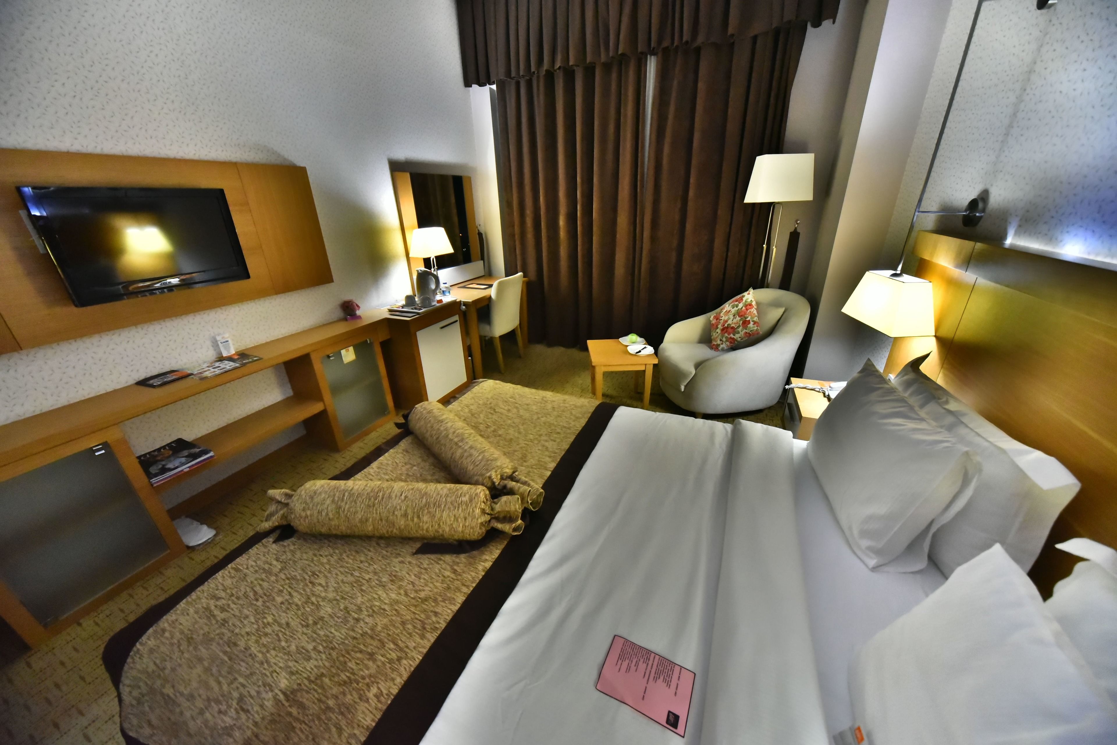 Una habitación de hotel con una cama, un escritorio, una silla, un televisor y una lámpara.