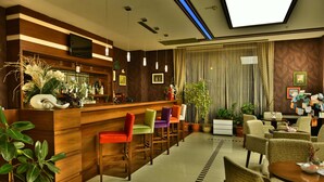 Een hotel lobby met een houten receptiebalie, kleurrijke barkrukken, potplanten en een zithoek met rieten stoelen.