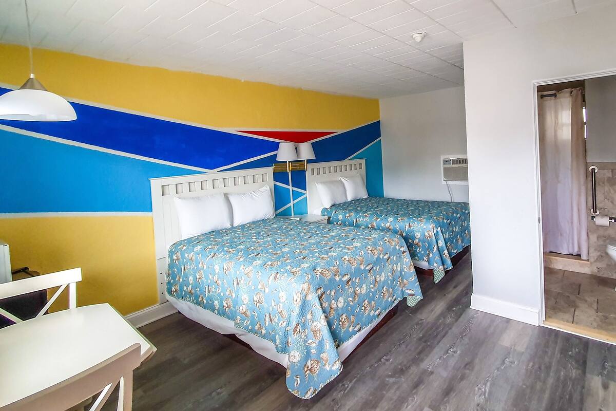 Een kamer met twee bedden, een bureau en een stoel. Er is een plafondlamp en een airconditioning.