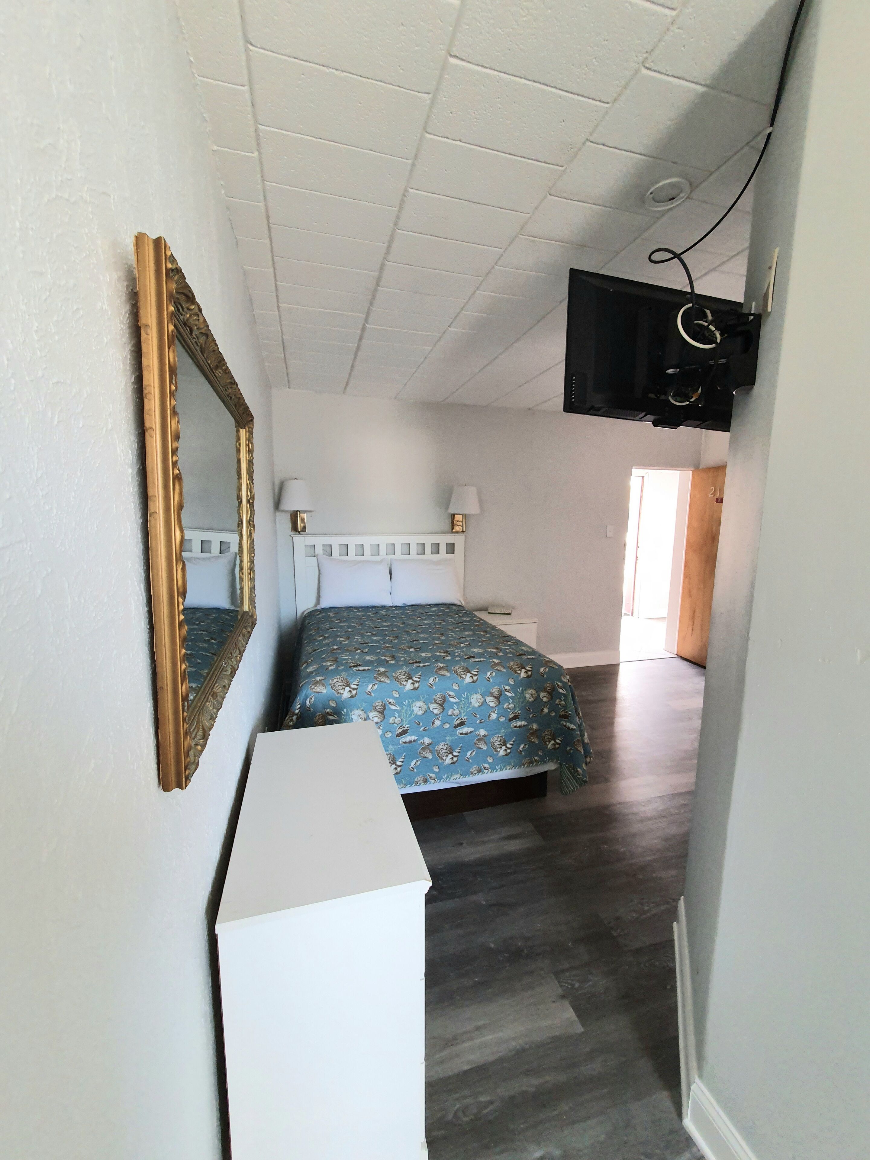 A bedroom with a bed, a dresser, a mirror, and a TV mounted on the wall.