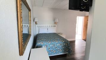 A bedroom with a bed, a dresser, a mirror, and a TV mounted on the wall.