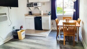 Una cocina compacta con gabinetes blancos, microondas y cafetera. Hay una mesa de comedor con sillas y una ventana con cortinas.