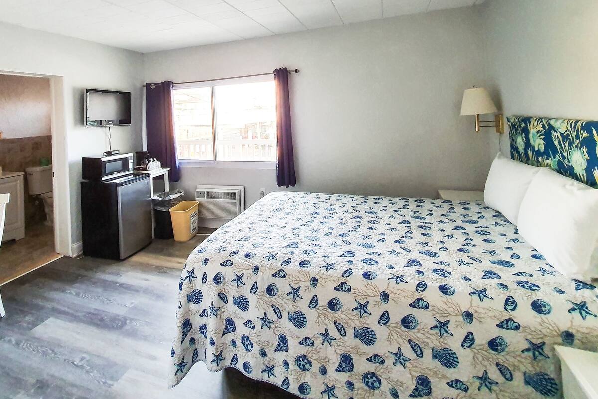 Een slaapkamer met een bed, een bureau, een stoel, een televisie en een raam met gordijnen.