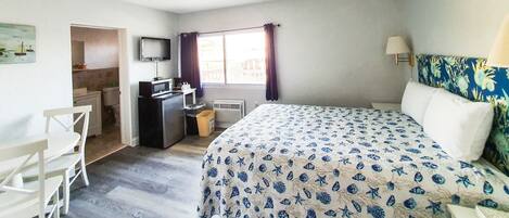 A bedroom with a bed, a desk, a chair, a TV, and a window with curtains.