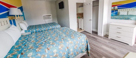 A bedroom with two beds, a white dresser, a mirror, and a door leading to a bathroom.