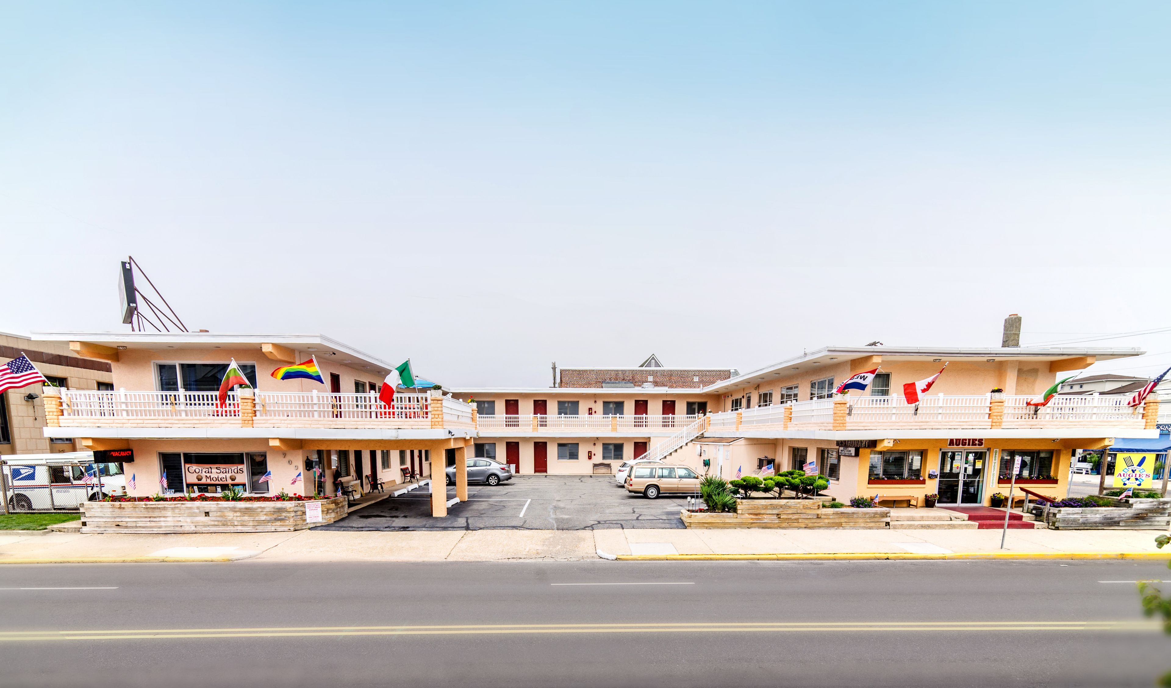 A motel with a two-story structure, a parking lot, and multiple flags.