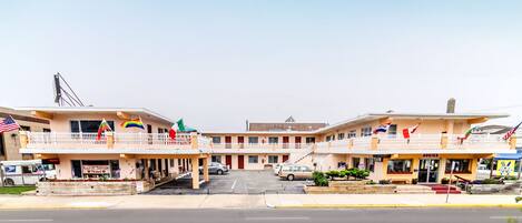 A motel with a two-story structure, a parking lot, and multiple flags.