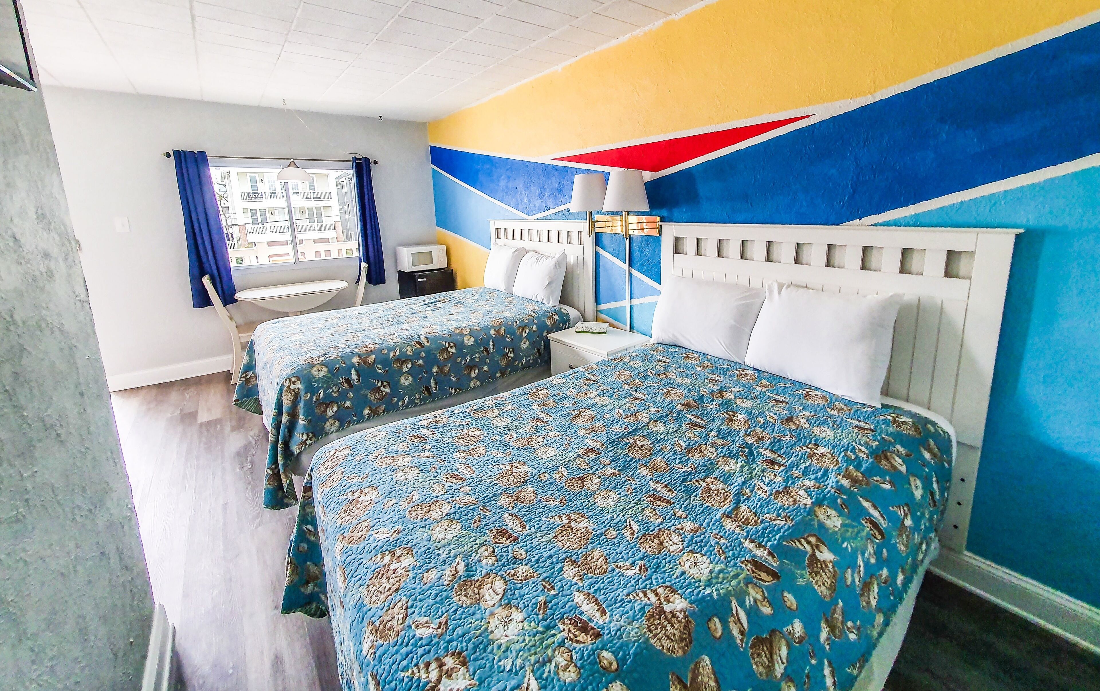 Habitación de hotel con dos camas, una mesita pequeña, una silla, un televisor y una ventana con cortinas.