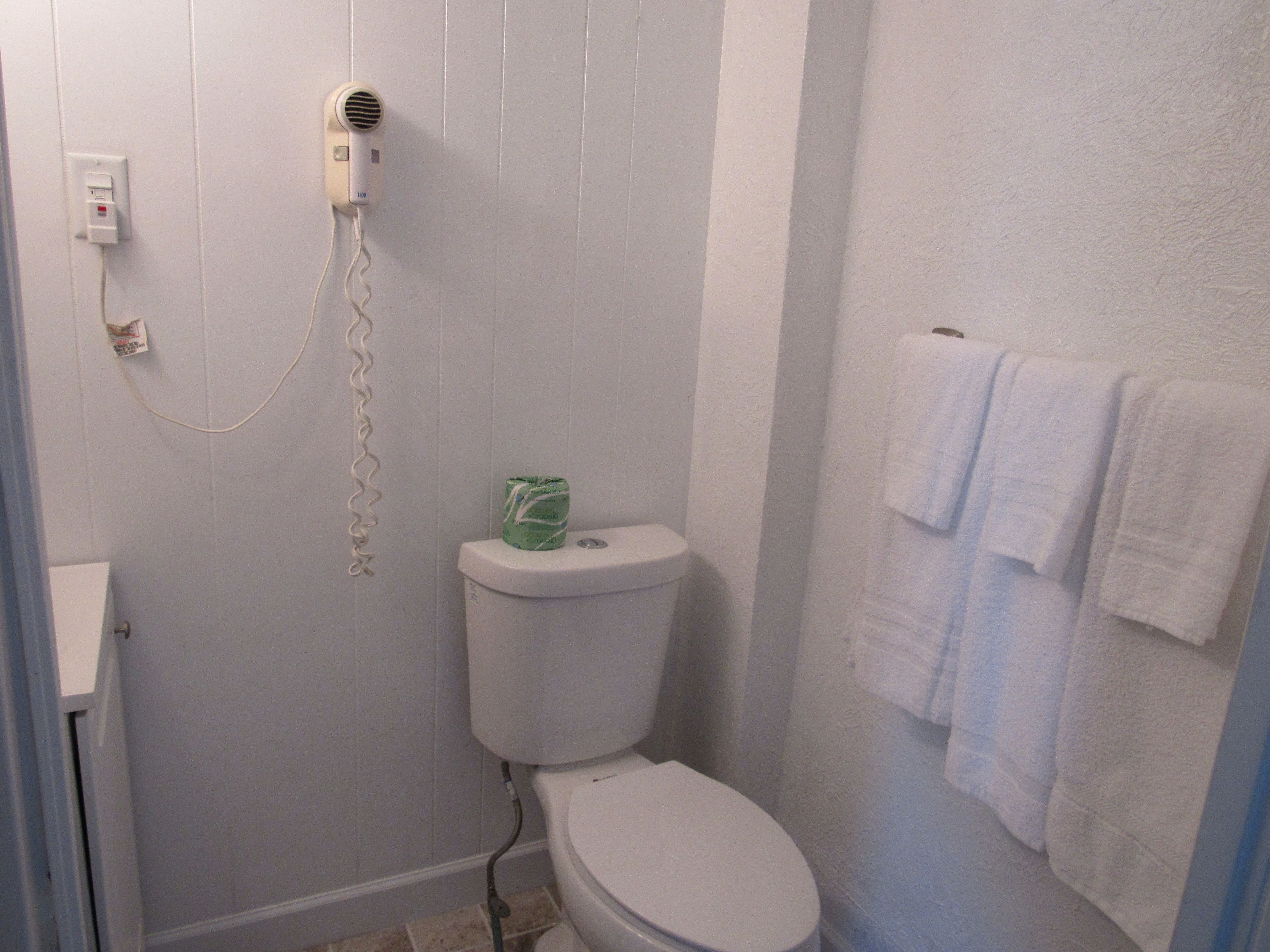 A bathroom with a toilet, a hairdryer on the wall, and a towel rack with towels.