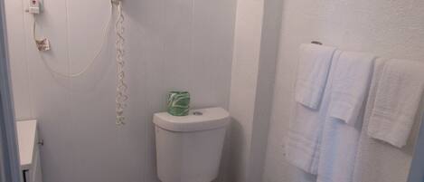 A bathroom with a toilet, a hairdryer on the wall, and a towel rack with towels.