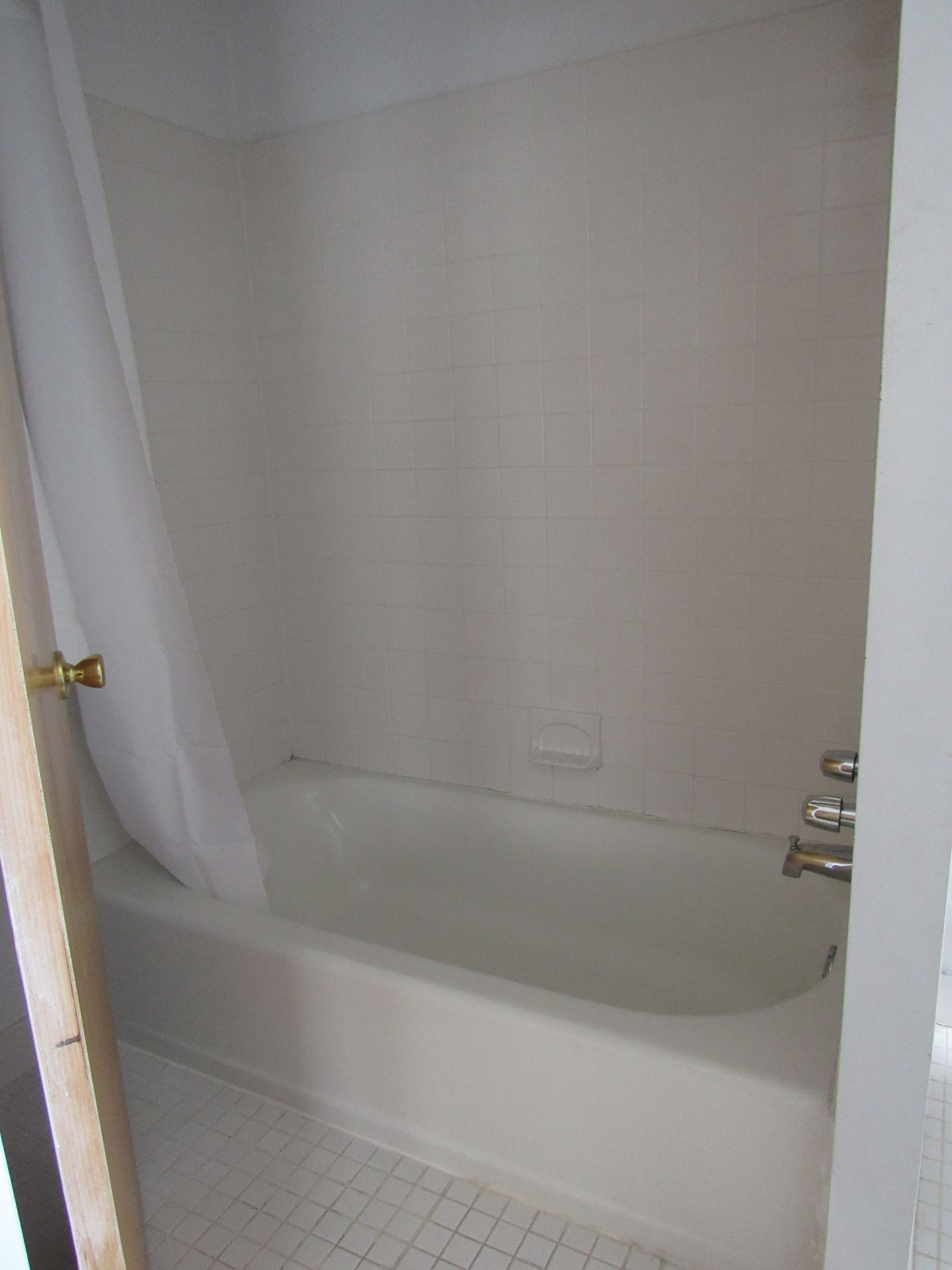 Un baño con bañera, paredes de azulejos blancos y cortina de ducha.