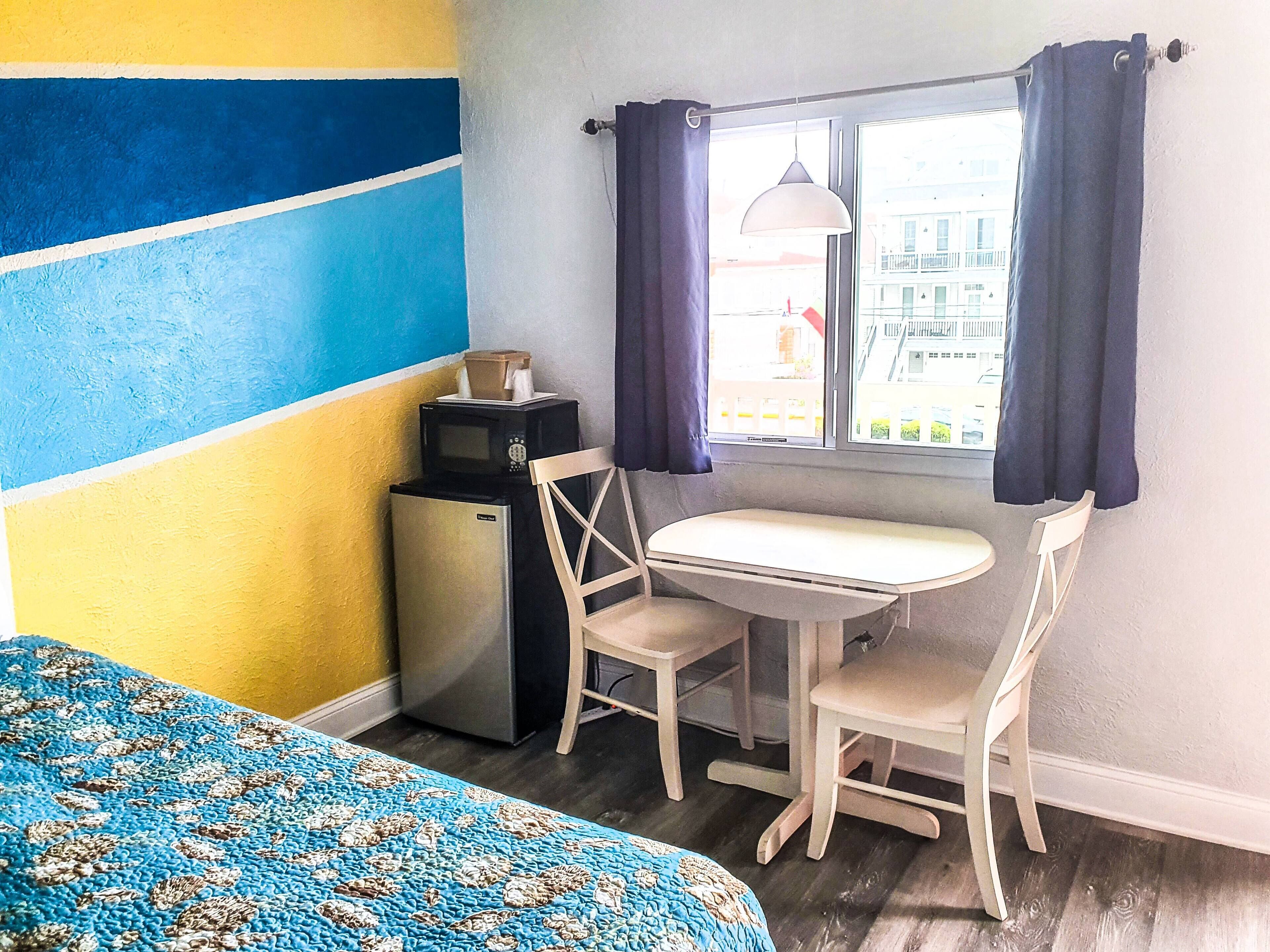 Une petite pièce comprenant un lit, une table, deux chaises, un four à micro-ondes et un réfrigérateur.