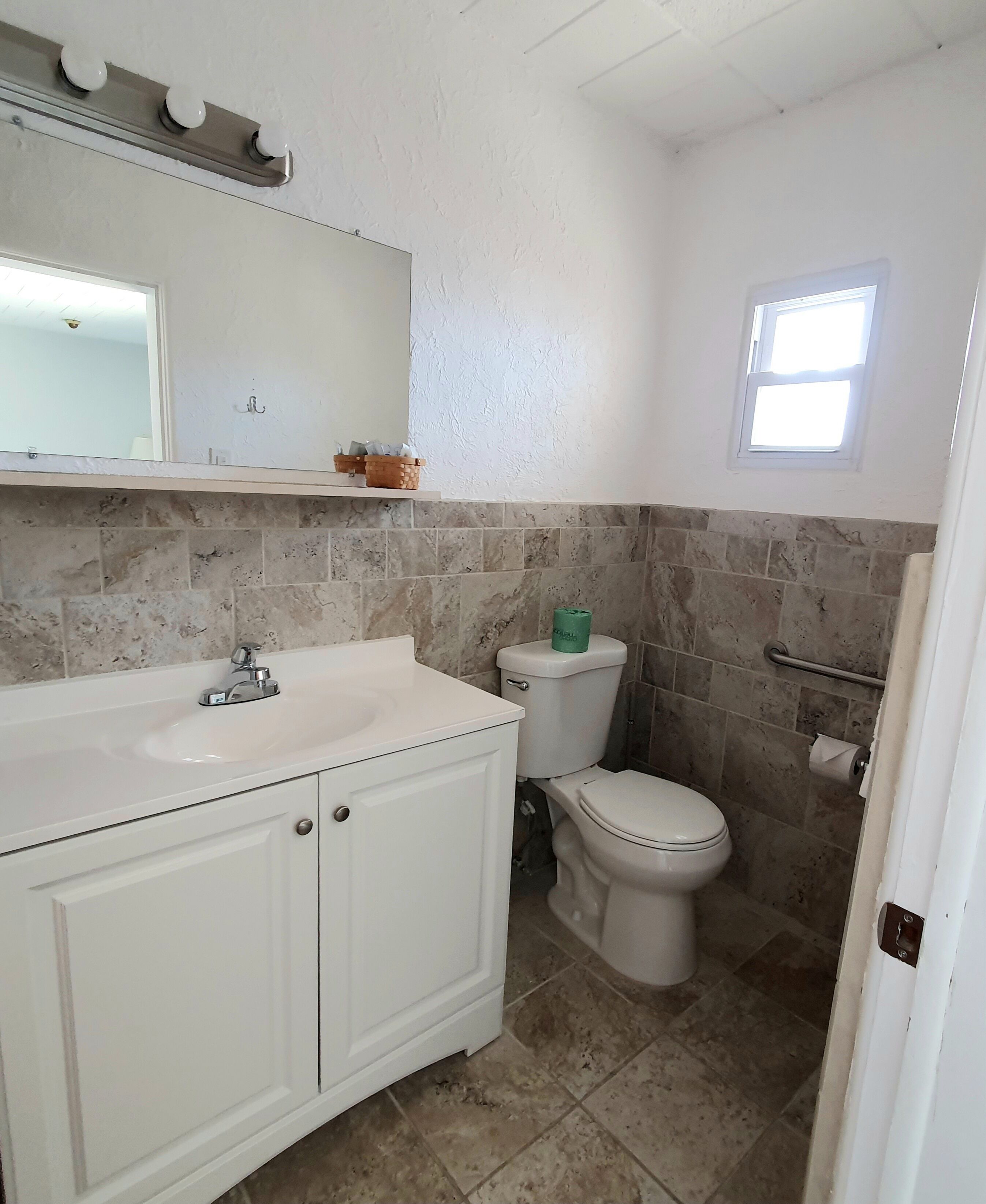 A bathroom with a white sink, a toilet, a mirror, and a small window.