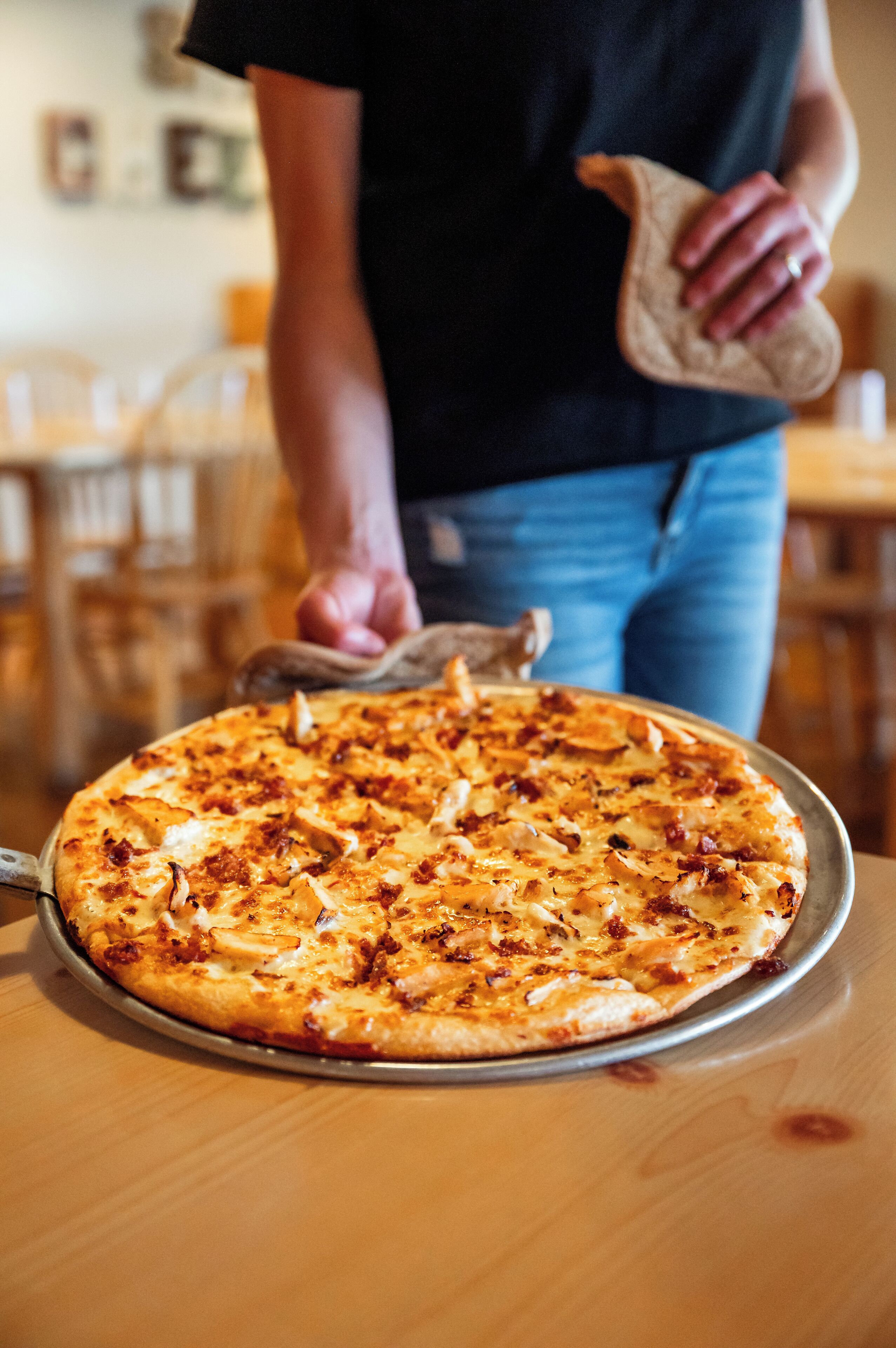 A pizza on a metal tray on a wooden table.