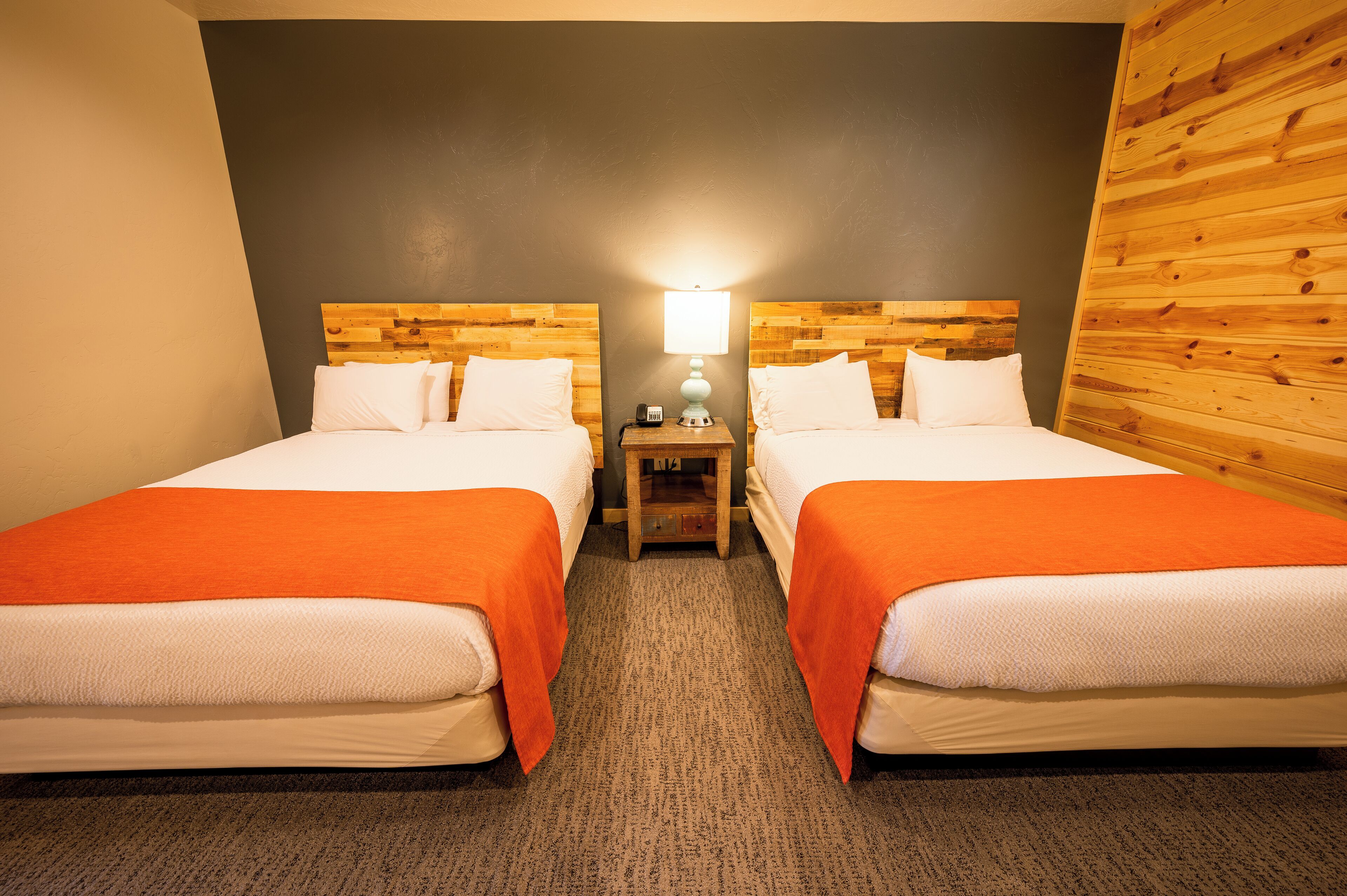 A hotel room with two beds, a nightstand with a lamp, and a wooden headboard.