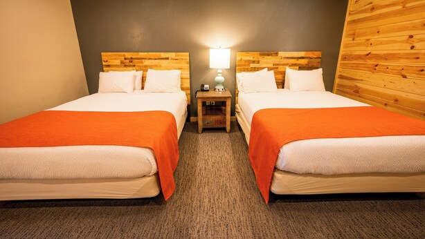 Una habitación de hotel con dos camas, una mesita de noche con lámpara y un cabecero de madera.
