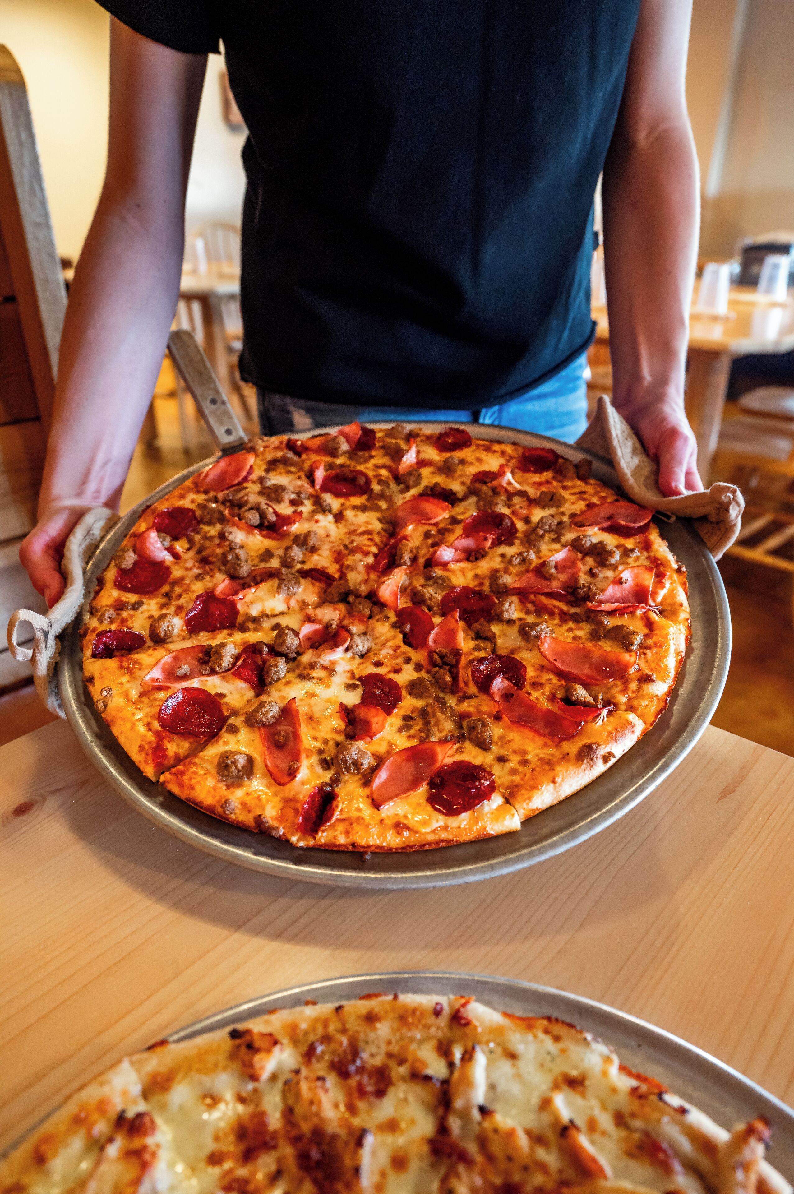 Une personne tenant une pizza garnie de pepperoni et de saucisses.