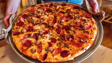 Une personne tenant une pizza garnie de pepperoni et de saucisses.