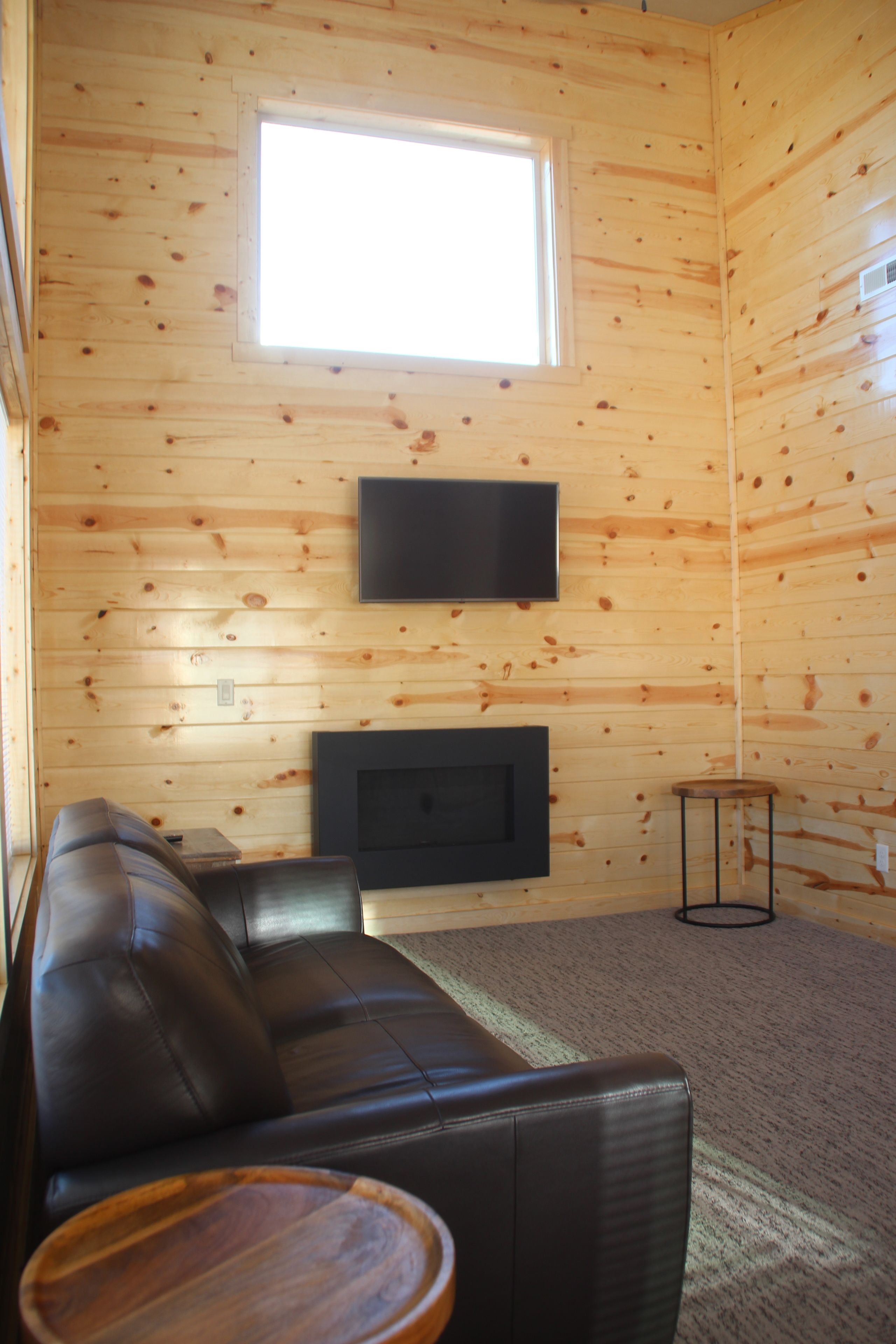 A log cabin interior with a leather sofa, a flat-screen TV mounted on the wall, and a fireplace below.