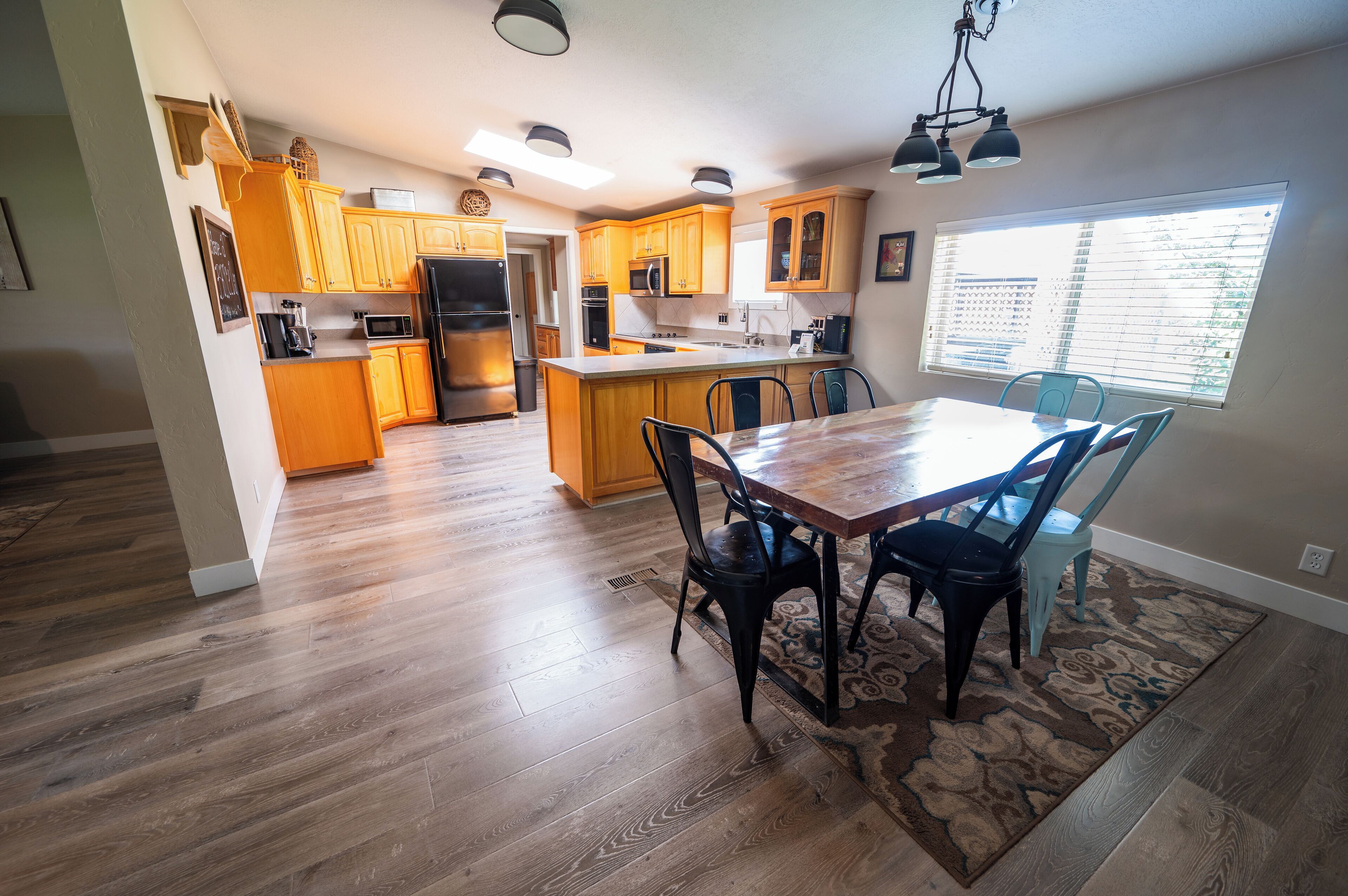 A modern kitchen with wooden cabinets, a central island, and a dining area with a table and chairs.