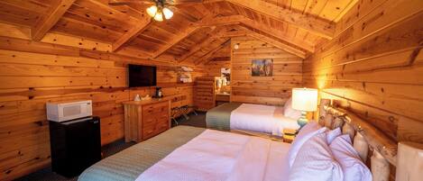 A cozy log cabin bedroom with two beds, a ceiling fan, a microwave, and a television.