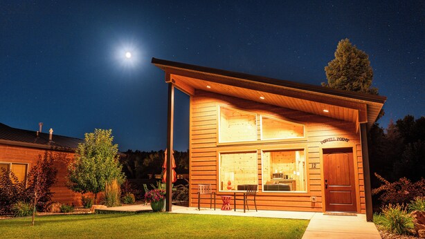 A two-story wooden house with a large window and a door, surrounded by a well-maintained lawn and trees. - Bryce Canyon Inn (Tropic)
