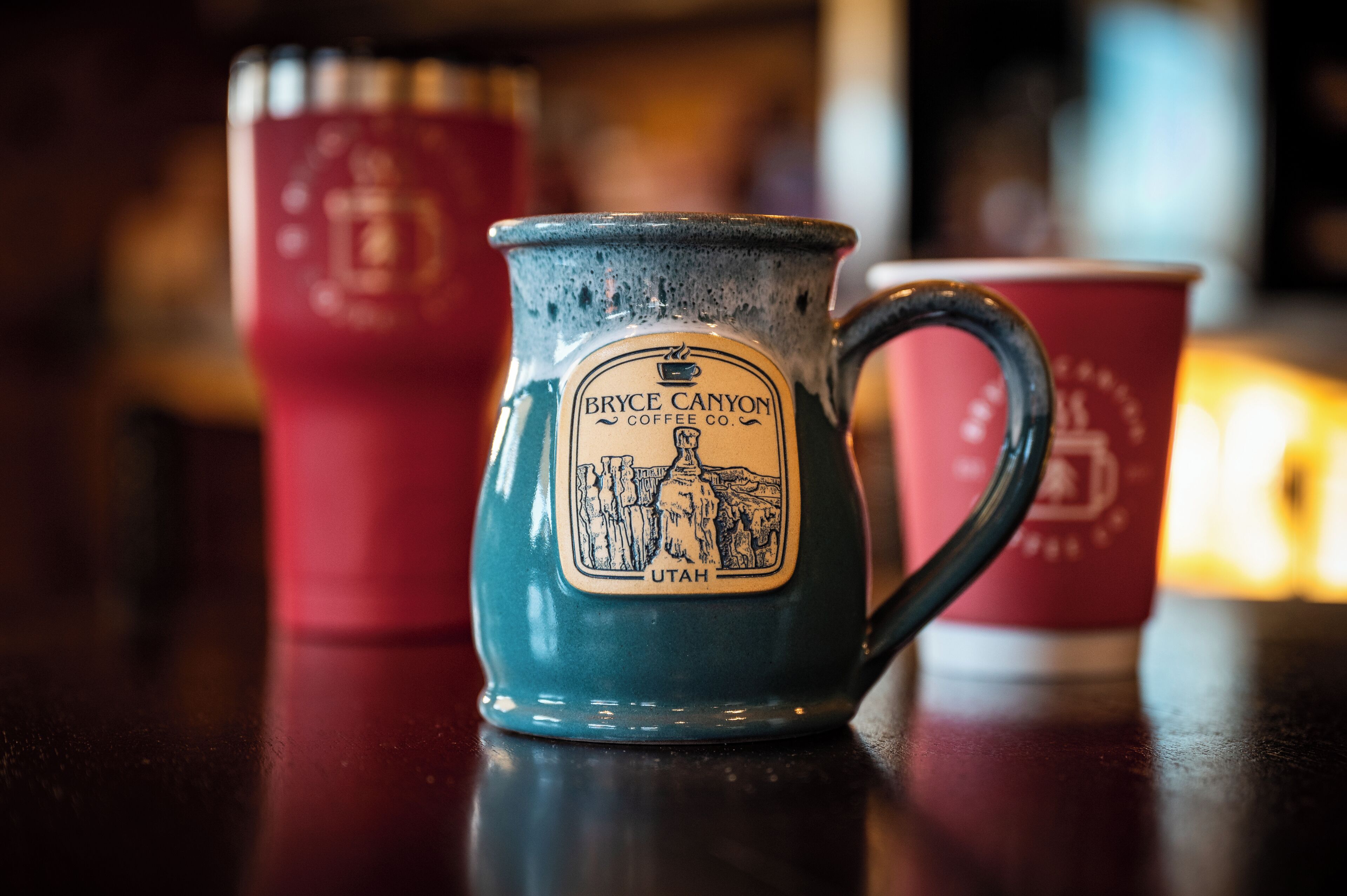 Eine blaue Keramiktasse mit dem Logo von Bryce Canyon Coffee Co. und einer roten Tasse im Hintergrund.