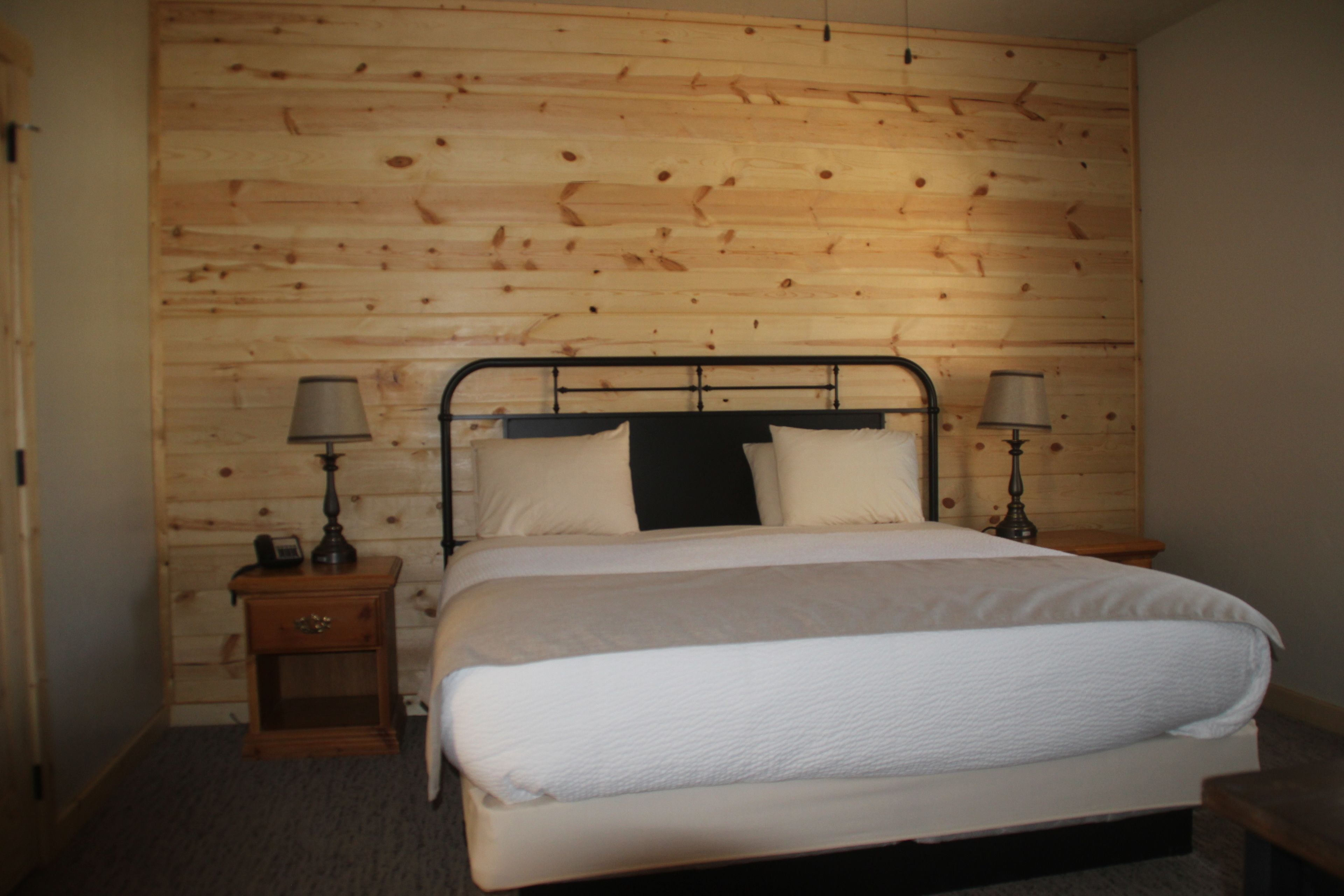A bedroom with a wooden headboard, a bed with white bedding, two bedside tables with lamps, and a small wooden nightstand.