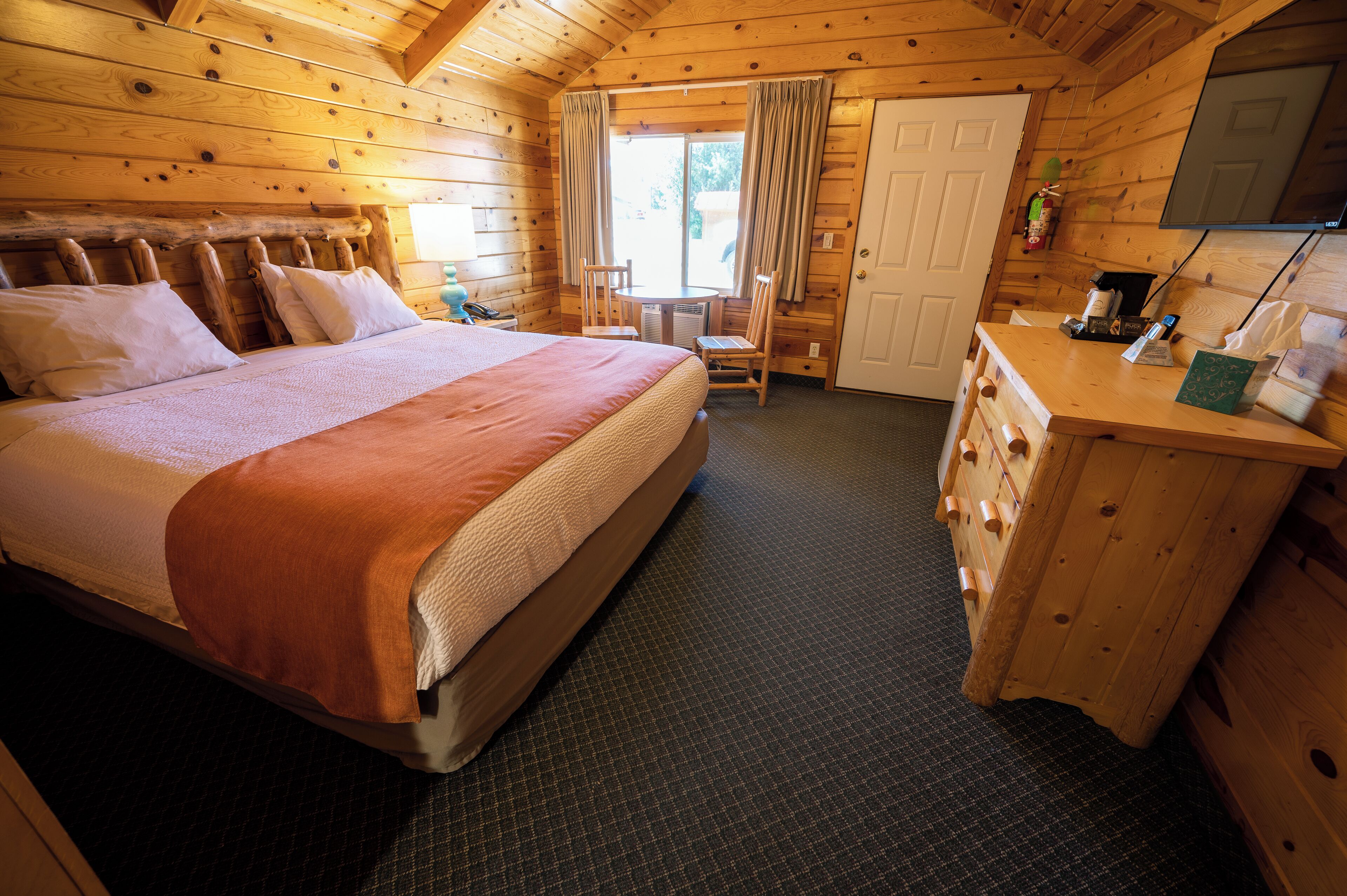 A wooden cabin room with a bed, a desk, and a chair.