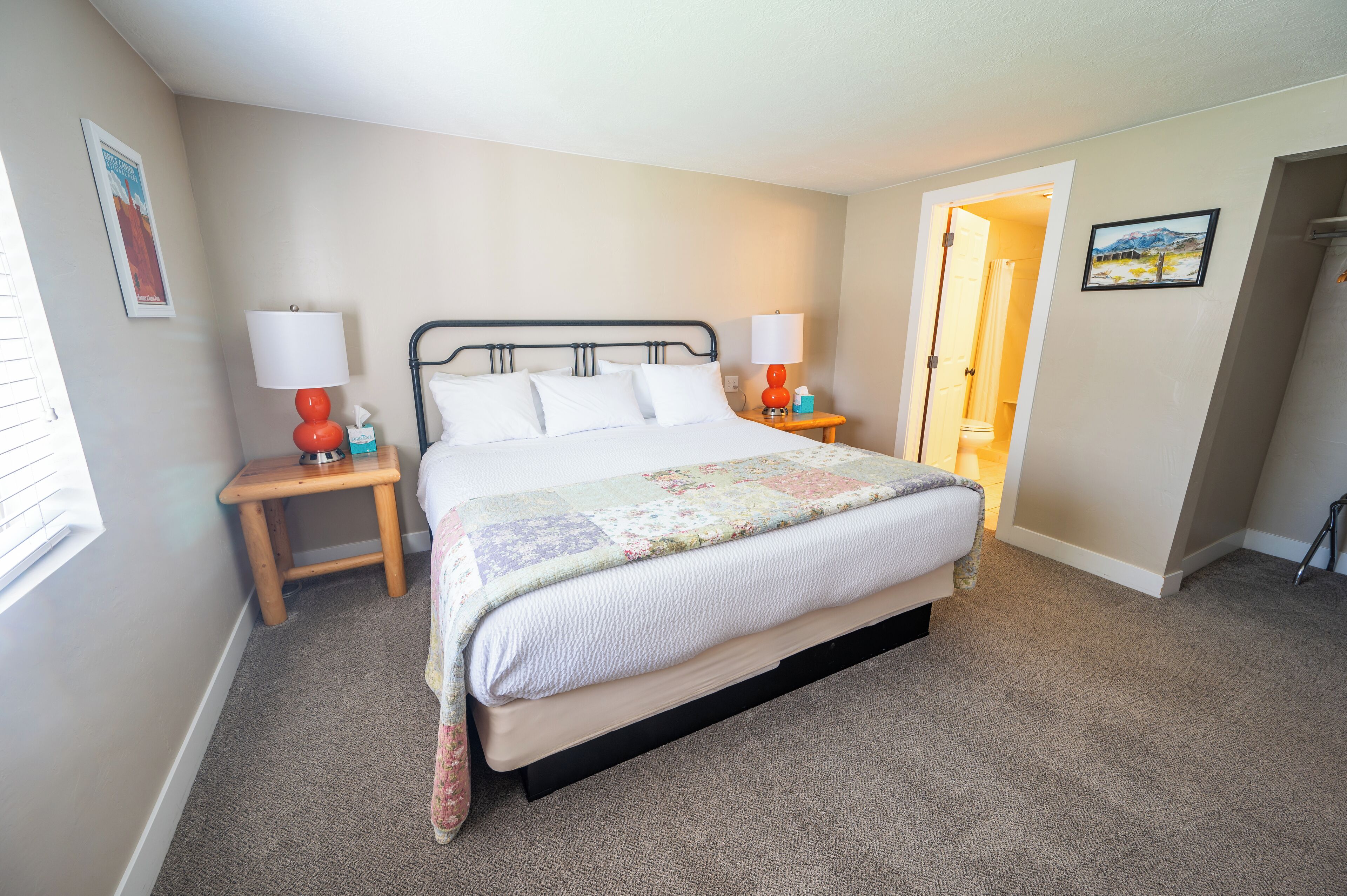 A bedroom with a bed, two bedside tables, a nightstand, a door, and a wall with a picture.