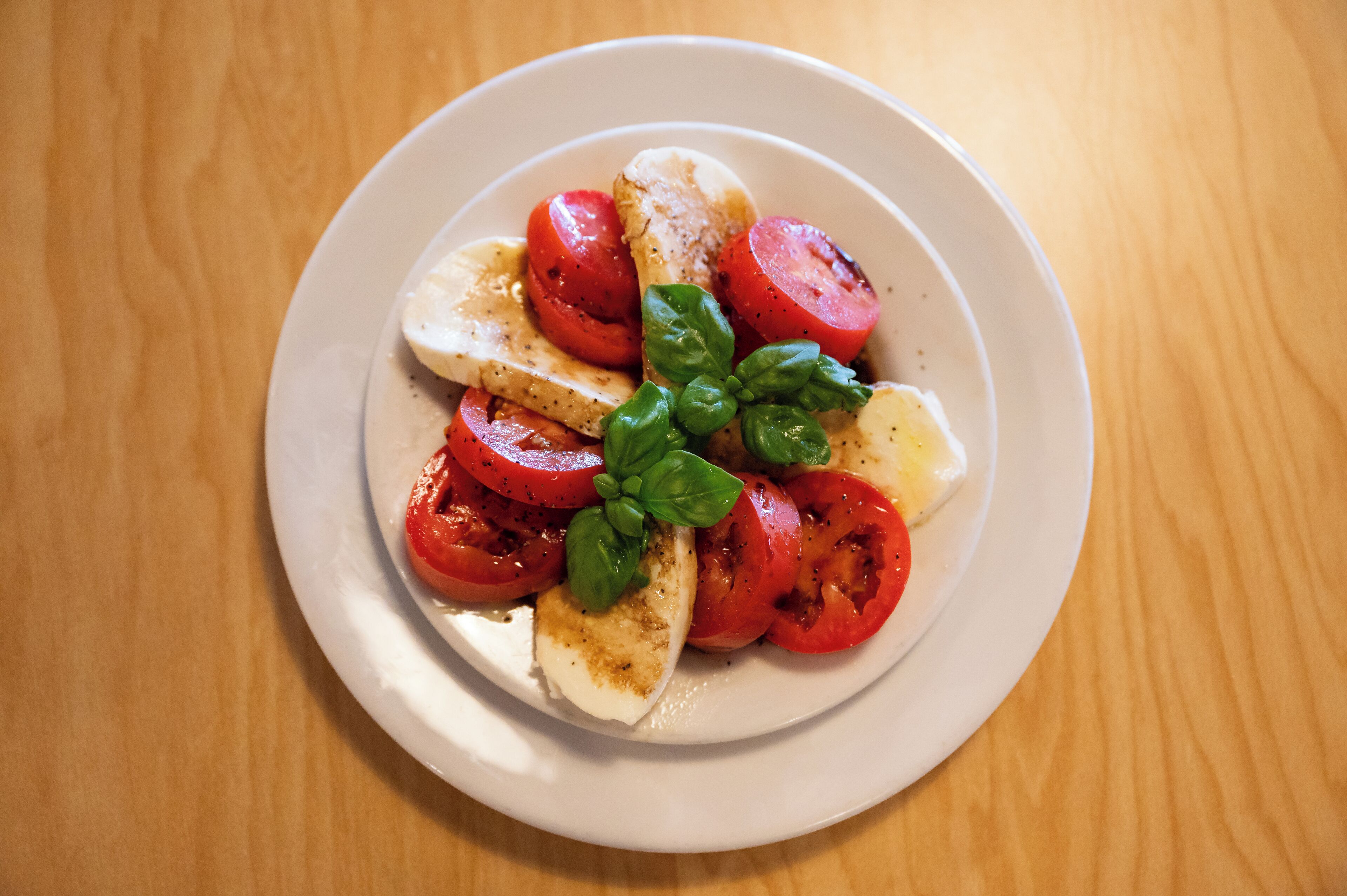 A plate of Caprese salad with tomatoes, mozzarella, and basil on a white plate.