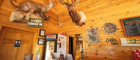 A rustic interior with wooden walls, a 'Guest Check In' sign, a 'Coffee Tea' sign, and a menu board.