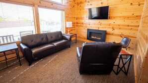 A cozy cabin-style room with a leather sofa, a television mounted on the wall, and a fireplace. - Bryce Canyon Inn (Tropic)