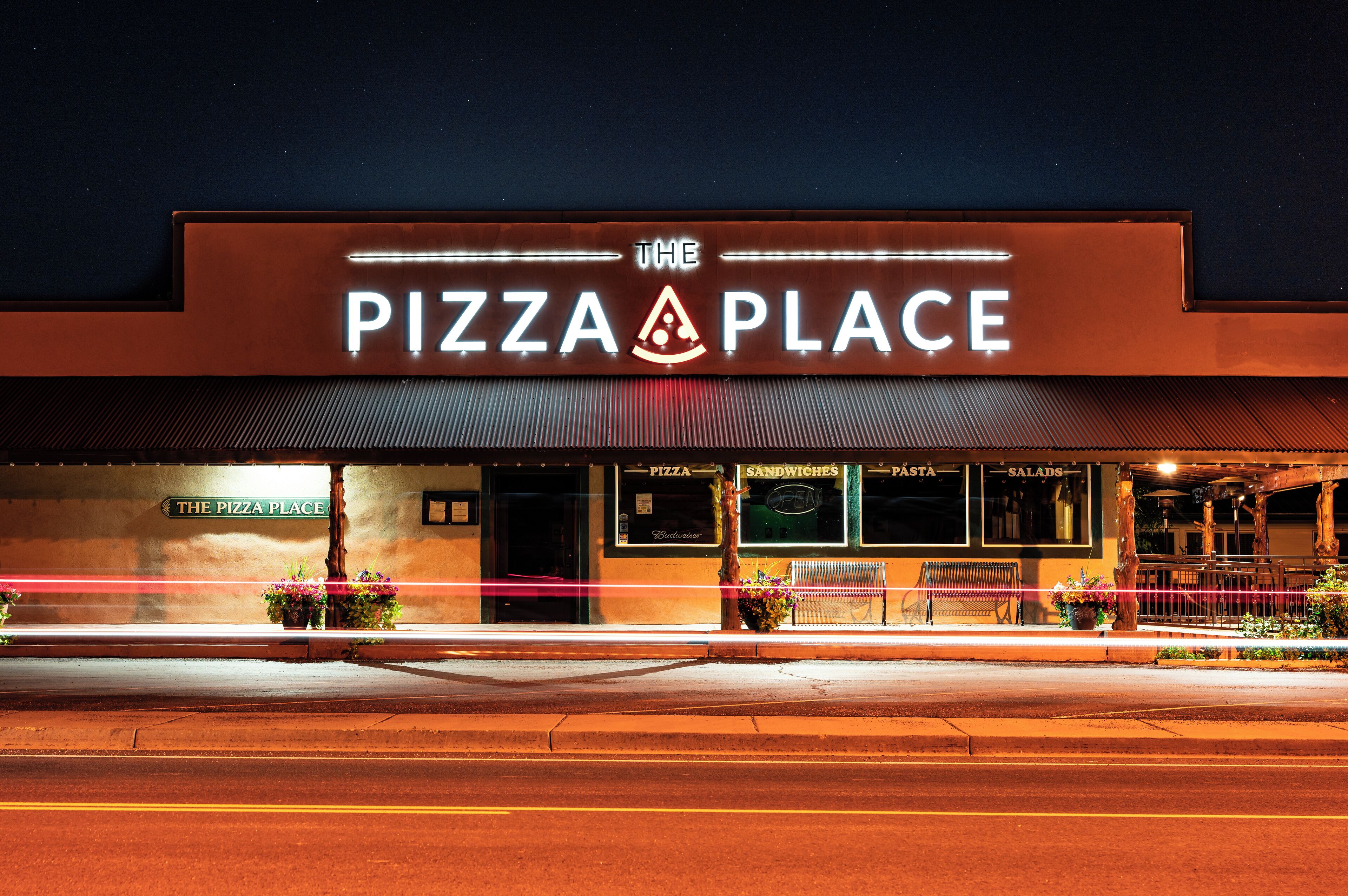 A restaurant named "The Pizza Place" with a signboard, outdoor seating, and a visible menu board.