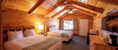 Et bjælkehytteværelse med to senge, træloft, ventilator, et lille bord og en mikrobølgeovn.