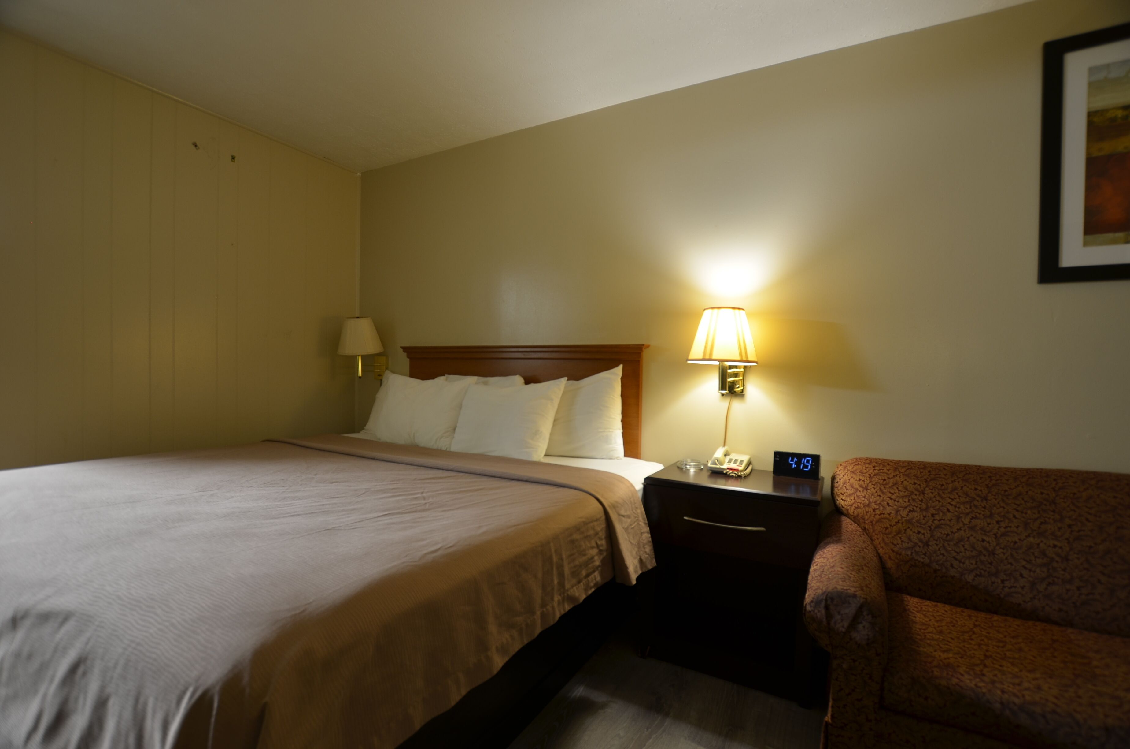 Une chambre d’hôtel avec un lit, une table de chevet avec une lampe et un canapé.