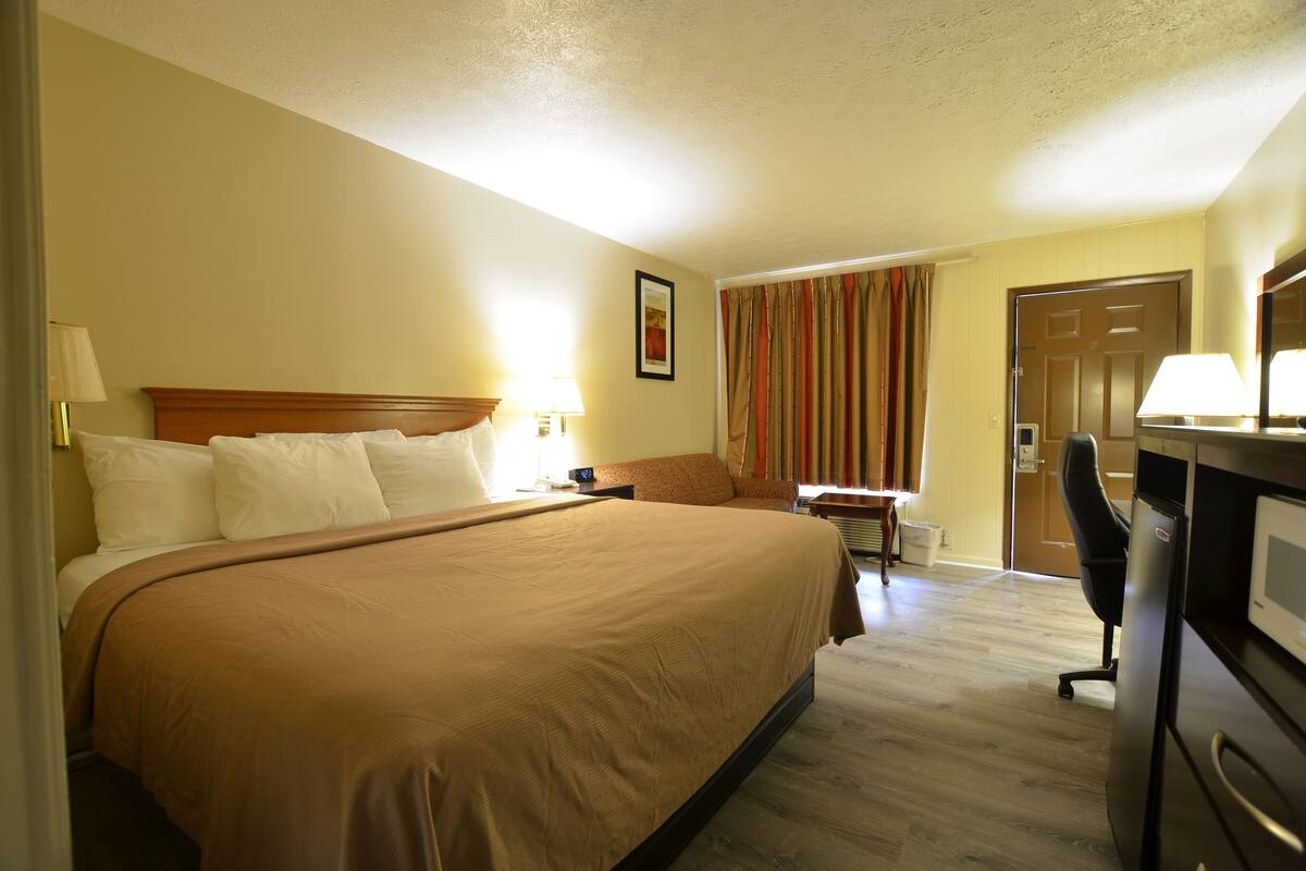A hotel room with a large bed, a desk, a chair, and a television.