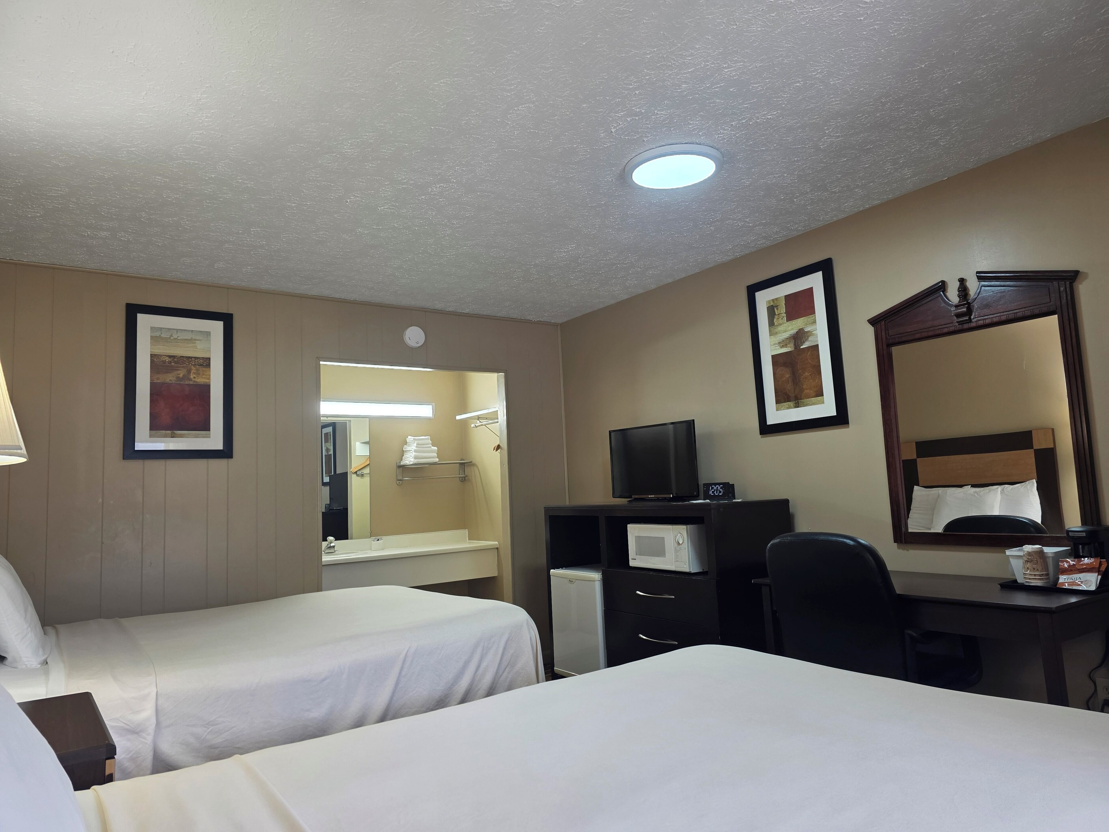 A hotel room with two beds, a desk with a computer, a television, and a mirror.
