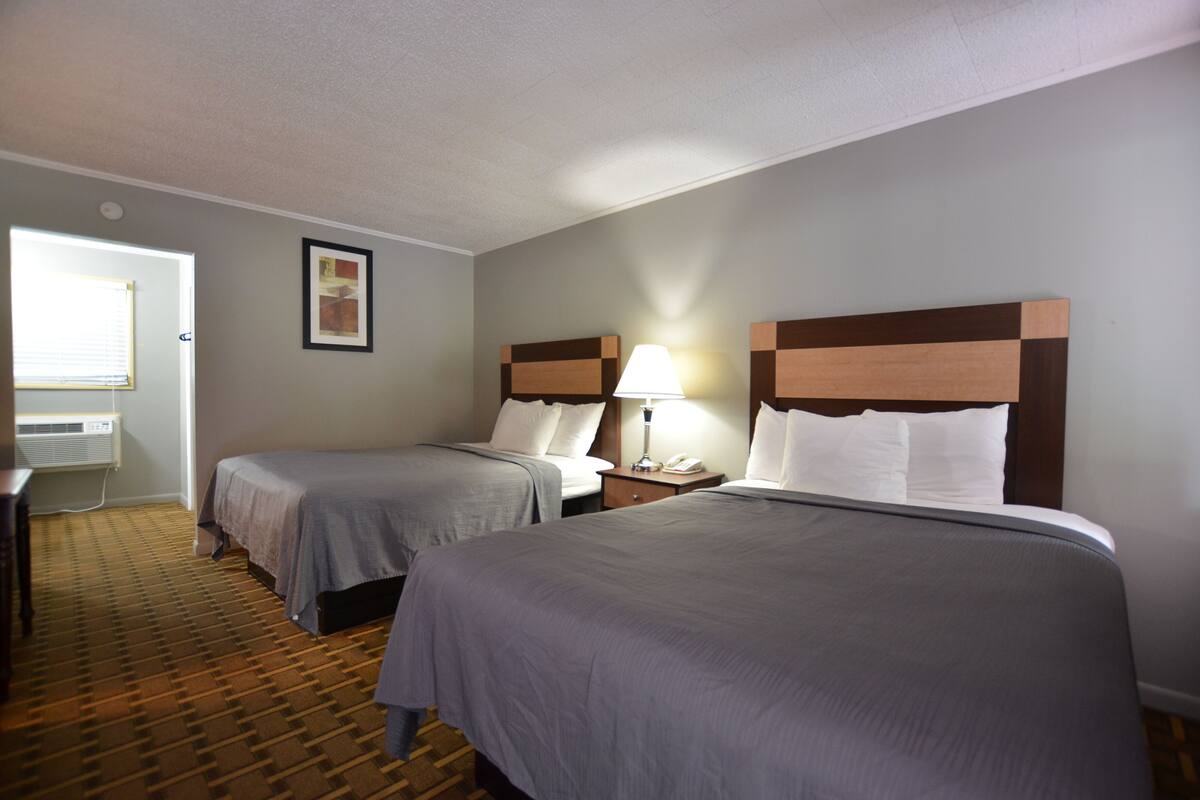 A hotel room with two beds, a desk, and a window.